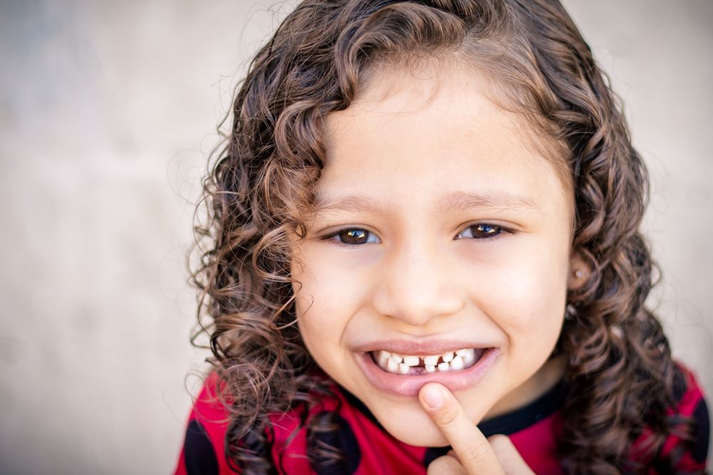 A happy child pointing to the gap where a baby tooth has fallen out