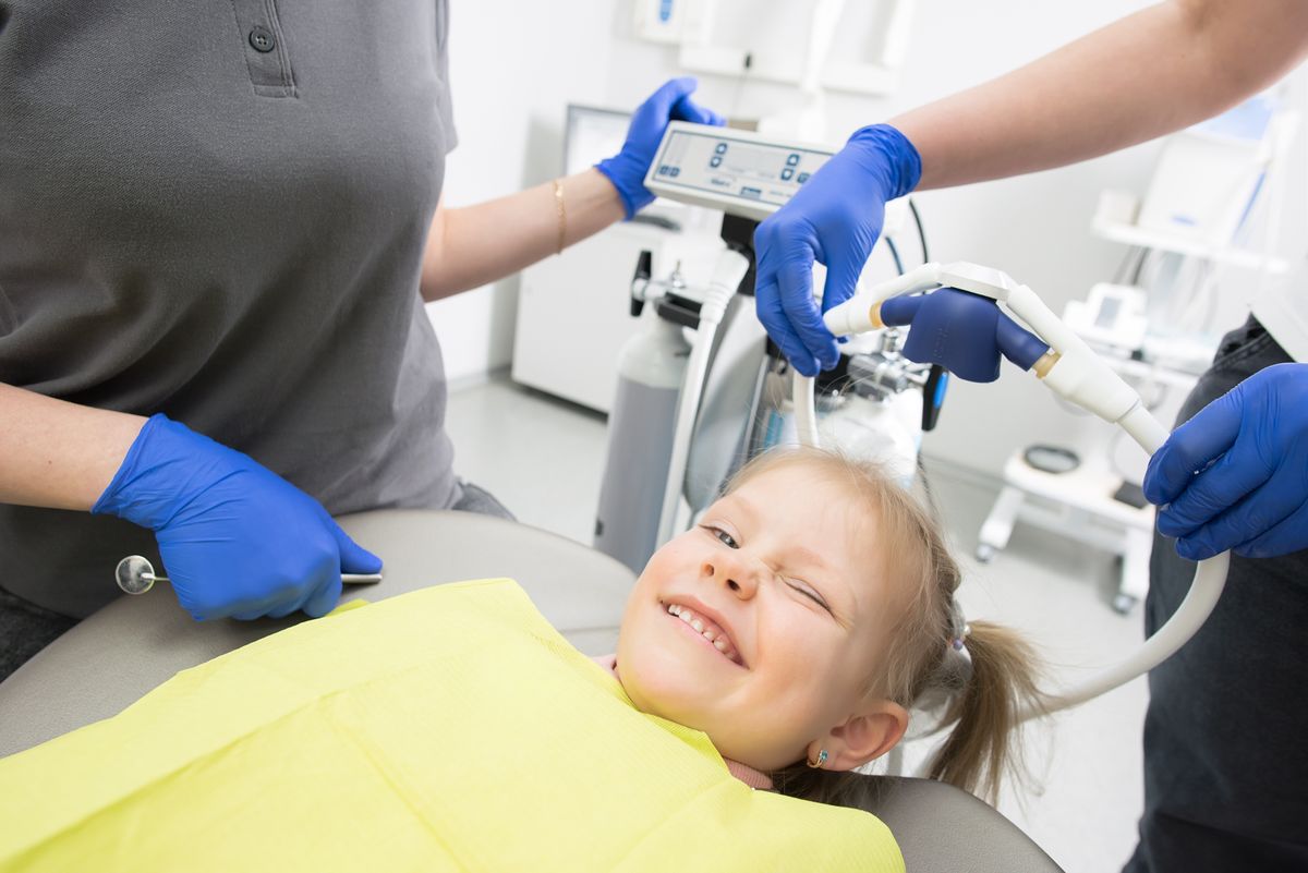 A smiling young girl in a dental chair with sedation equipment nearby before a pediatric procedure
