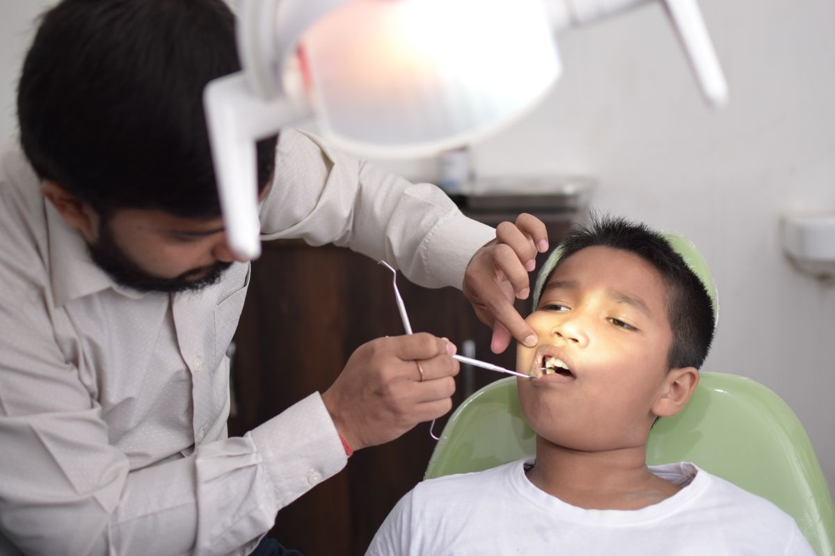A dentist gently examining the teeth of a young child at an early dental visit
